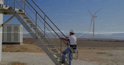 Wind turbine technician climbing staircase in rugged terrain