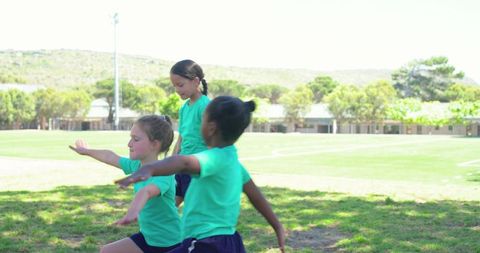 African american girls performing warmups on school sports field in teal shirts