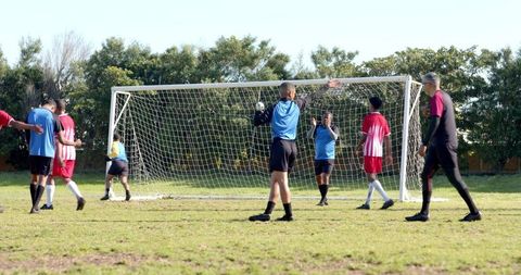 Diverse Male Soccer Players Competing Near Goalpost on Sunny Day