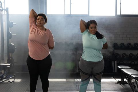 African american women stretching triceps together in industrial gym with dumbbells