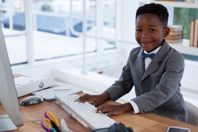 Young boy dressed in a suit working on a computer in a modern office. Ideal for concepts related to young professionals, future leaders, education, business training, and technology use among children. Can be used in educational materials, business training programs, and advertisements promoting children's educational tools.