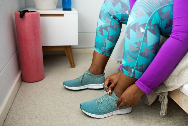 Low section of african american woman in sportswear tying shoes. health and fitness at home in self isolation during coronavirus covid 19 pandemic.