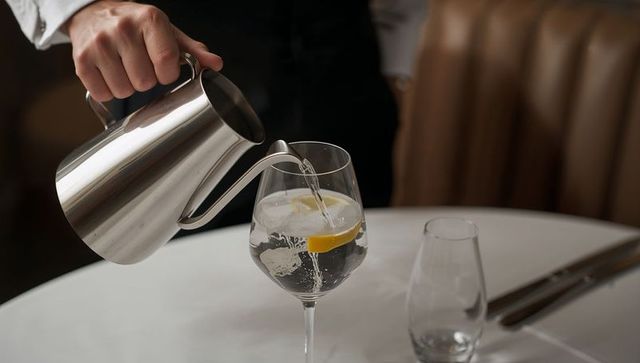 Waiter pouring water with lemon into wine glass using gooseneck pitcher in fine dining
