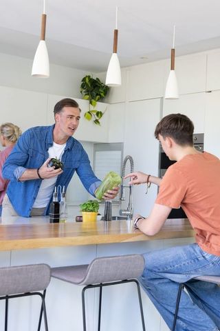 Father and teen preparing salad at modern kitchen island handing lettuce by faucet