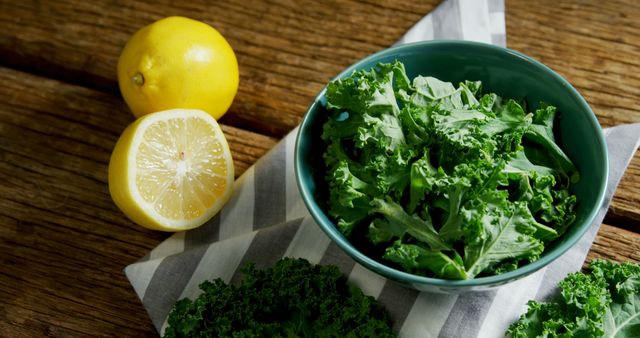 A bowl of fresh, chopped kale sits on a wooden table next to a whole lemon and a sliced half, with copy space. Kale is known for its health benefits, and adding lemon enhances its flavor and vitamin content.