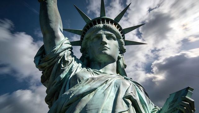 Towering statue of liberty close-up showing crown torch and tablet against dramatic cloud-filled sky
