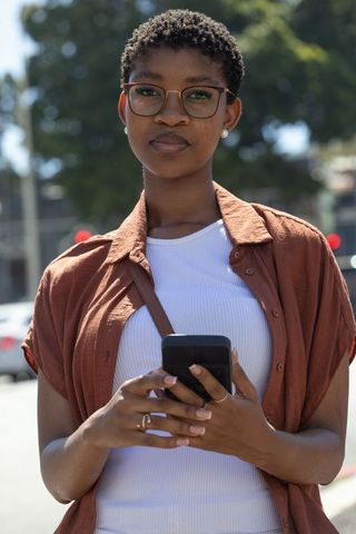 African american woman standing on city street holding smartphone, casual urban portrait