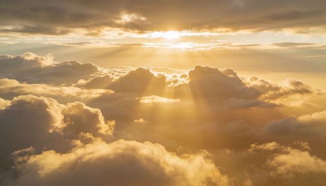 Golden sunbeams piercing layered clouds at sunrise over aerial horizon