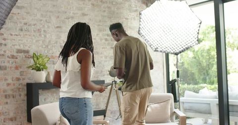 Diverse creative team adjusting lighting and camera in cozy living room studio