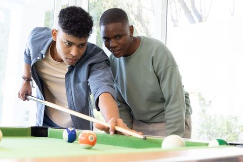 African american teenage boys practicing billiards shot in sunlit modern game room