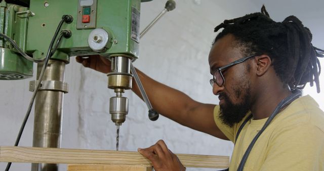 African American man operates a drill press in a workshop. Skilled craftsman focuses on precision in his woodworking project at home.