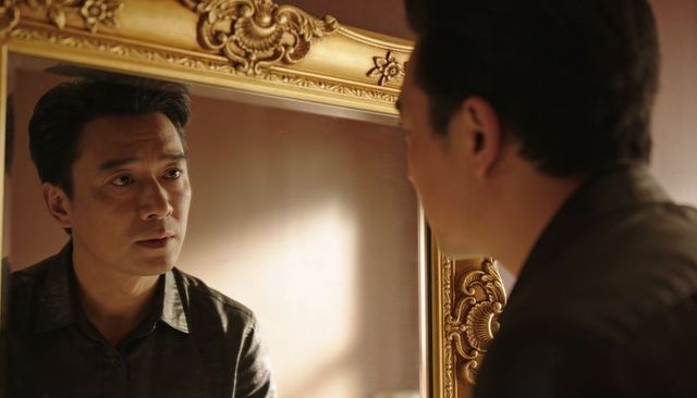 Man studying reflection in ornate gold mirror contemplating in warm hotel interior