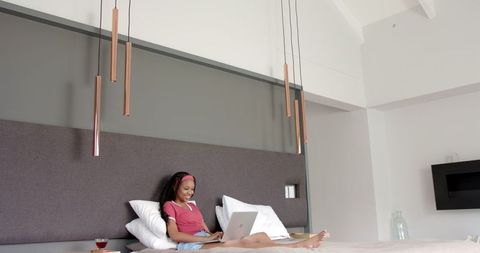 African American Woman Relaxing on Bed with Laptop at Home