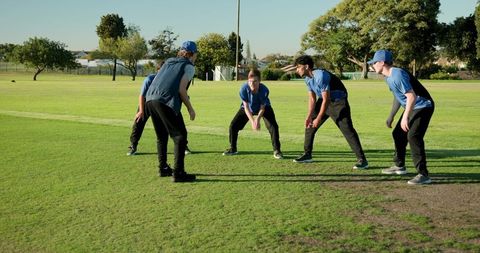Coach underhand tossing ball while youth cricket team practicing fielding drill on grass