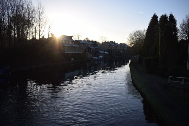 Sunset over a calm canal reflecting houses and trees in a tranquil village. This image captures the peaceful and serene environment perfect for themes of relaxation, nature, and rural life. Suitable for travel blogs, nature websites, and promotional materials for retreats.