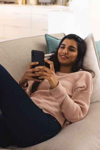 Young Woman Relaxing on Sofa with Smartphone Indoors