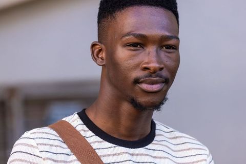 Young man standing wearing striped knit sweater and brown shoulder bag casual headshot