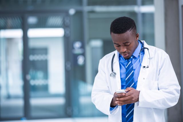 Doctor standing in hospital corridor using mobile phone. Ideal for illustrating modern healthcare, medical technology, and professional communication in medical settings. Useful for healthcare apps, medical websites, and professional healthcare promotions.