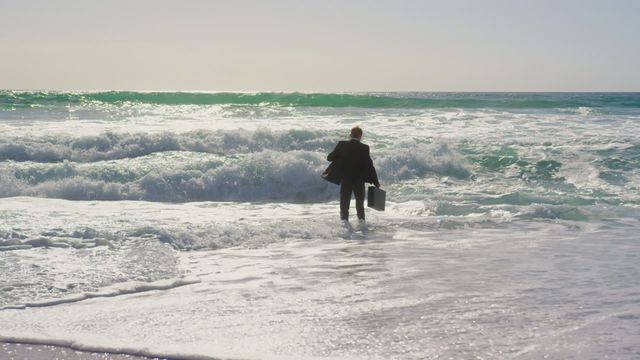 A young businessman in a suit with briefcase walking towards ocean waves on a sunny day. This video is ideal for concepts of career transformation, determination, business travel, work-life balance, or new beginnings. It can be used in business presentations, motivational content, website banners, or articles focusing on professional growth and adventure.