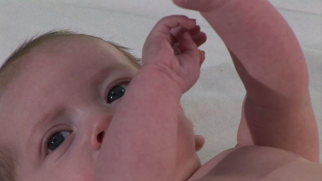 The image shows a close-up view of a baby with expressive eyes, lying down and reaching out. This image is perfect for family and childcare-related content, baby product advertisements, or parenting blogs. Its intimate and heartwarming feel makes it an ideal choice for promoting baby care and parenting advice.