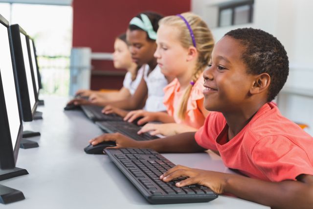 Group of elementary school children of different ethnicities using desktop computers in a classroom setting. Suitable for educational materials, technology in education articles, or school brochures promoting diversity and modern teaching methods.