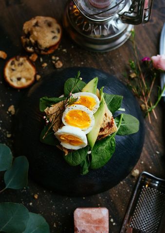 Soft-Boiled Egg Avocado Toast on Rustic Sourdough with Spinach and Herb Garnish