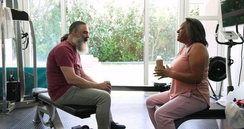 Senior couple relaxing with smoothies in home gym after workout