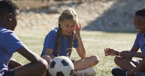 Diverse youth soccer teammates sitting on grass sharing laugh around soccer ball