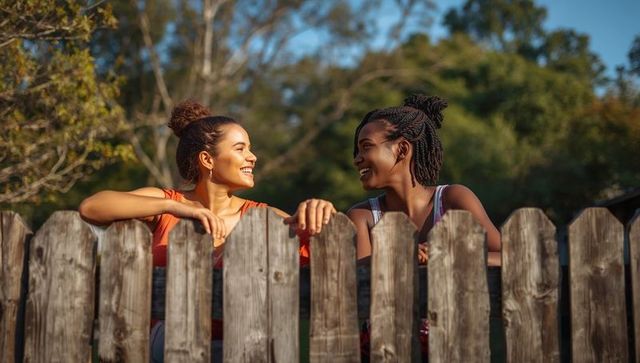 Two women chatting over picket fence on sunny day