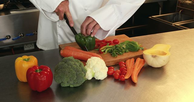 Chef chopping green bell pepper with various fresh vegetables including broccoli, carrots, and cauliflower on kitchen counter. Suitable for food blogs, culinary education, restaurant promotions, and health-focused content.
