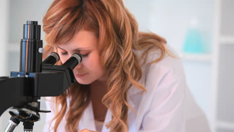 Focused Young Scientist Observing Under Microscope in Laboratory