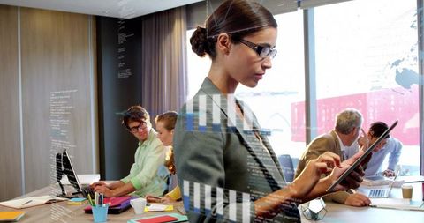 Businesswoman reviewing tablet with digital analytics while collaborative team working nearby