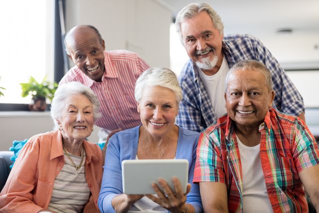 Group of smiling senior individuals gathered around a digital tablet in a nursing home. They are enjoying technology and spending time together. Perfect for illustrating themes of senior living, technology use among the elderly, and social interaction in retirement communities.