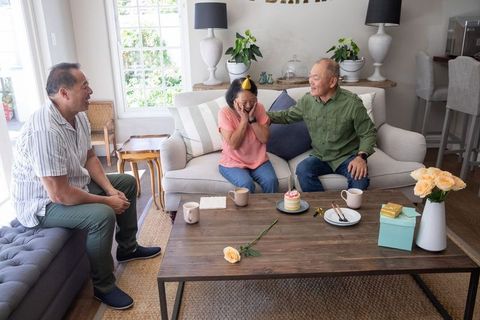 Surprised senior asian mother celebrating birthday with adult sons in cozy living room
