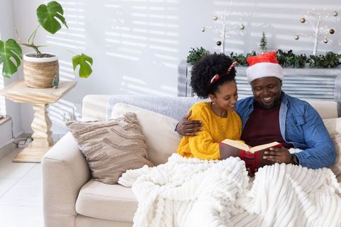 African american father and daughter reading together, sharing blanket and santa hat