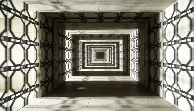 Receding framed atrium with geometric lattice shadows creating infinite light tunnel