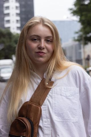 Young woman standing on city street wearing white button-up and brown leather crossbody bag