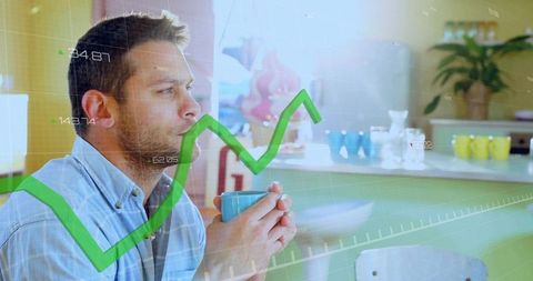 Contemplative man holding turquoise mug studying rising green stock graph at kitchen