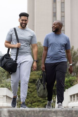 African american men walking and laughing on urban pedestrian bridge carrying duffel bags