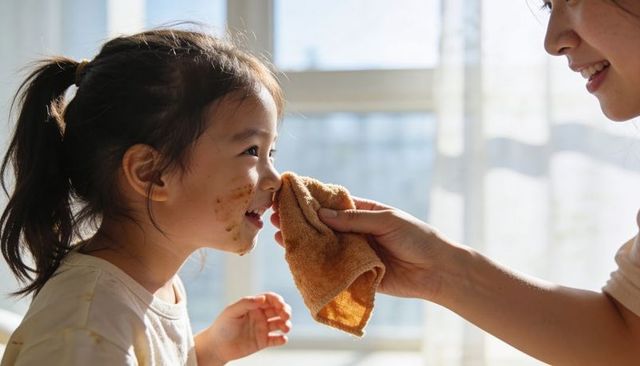 Mother wiping child chocolate-stained face with towel in sunlit tender family moment