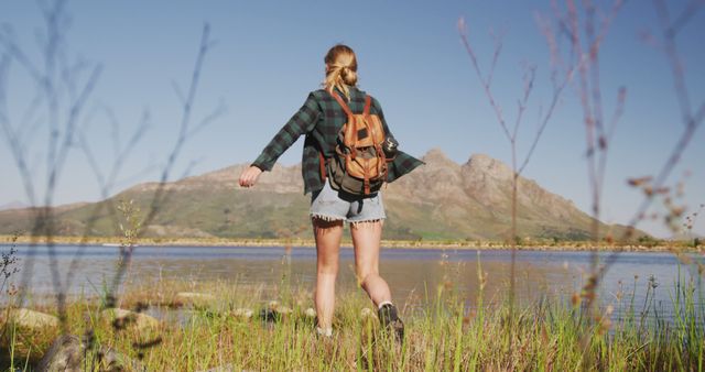 Woman is hiking near a clear mountain lake under a blue sky. Ideal for themes of outdoor adventure, solo travel, nature exploration, and peaceful retreats. This can be used for travel blogs, advertisements, magazines focused on wilderness adventures, and content promoting health and wellness through nature activities.
