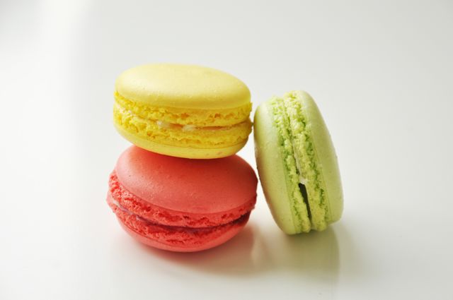 Colorful French macarons sitting on white background, showcasing a yellow, green, and red macaron piled atop each other. Ideal for use in bakery promotions, dessert menus, food blogs, or culinary arts advertisements.