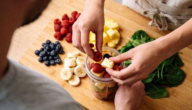Couple preparing fresh fruit spinach smoothie in personal blender cup on wooden board