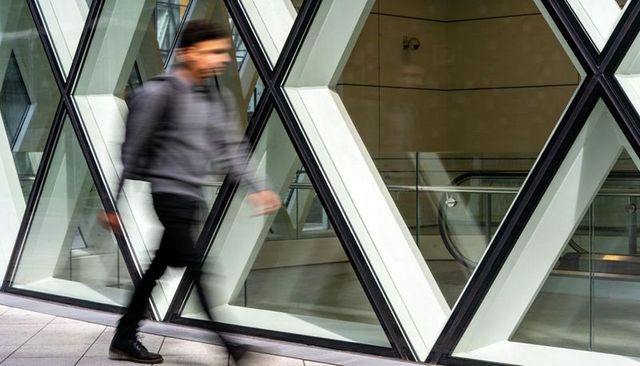 Walking commuter blurring past diamond glass facade with escalator and modern interior