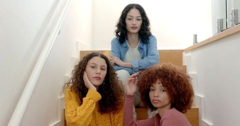 Three young women sitting on wooden stairs wearing knit sweaters and denim jacket