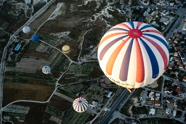 Aerial view featuring several colorful hot air balloons floating over a juxtaposed landscape comprising rural fields and urban areas. Effective for use in travel blogs, adventure adverts, tourism brochures, sky and landscape photography portfolios.