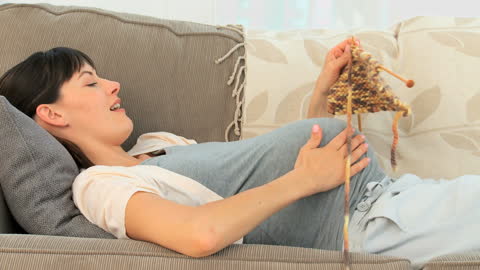 Pregnant Woman Knitting Relaxing on Sofa at Home