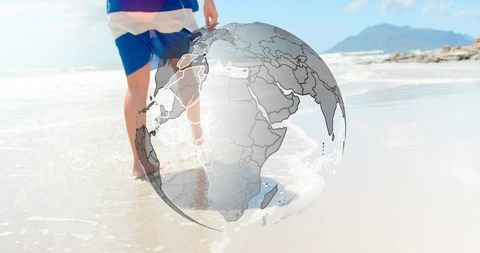 Walking barefoot on sunlit beach with transparent globe overlaying world map