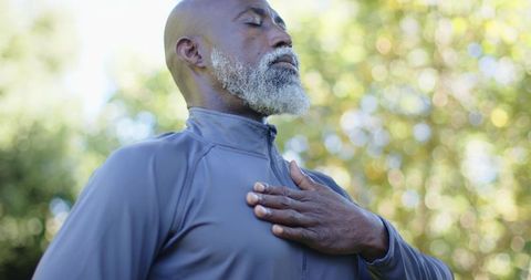 Senior african man practicing mindful breathing outdoors, hand on chest, promoting calm
