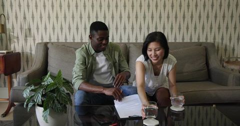Couple reviewing documents on sofa while sharing water in midcentury living room